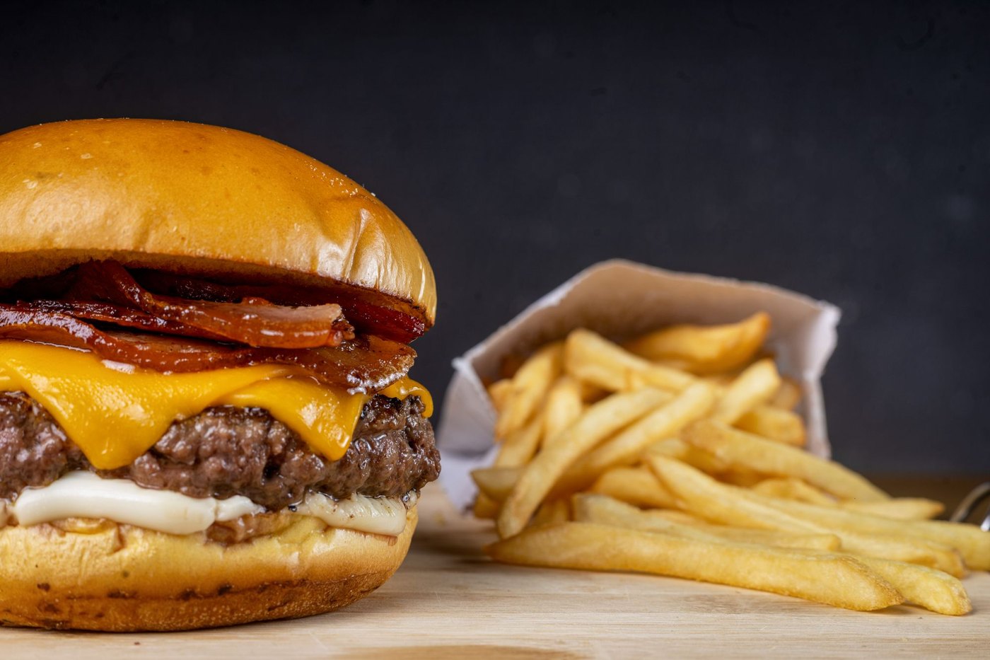 Licensed stock photograph: a bacon cheeseburger with melted cheese on a soft bun, a paper cone of fries beside it.