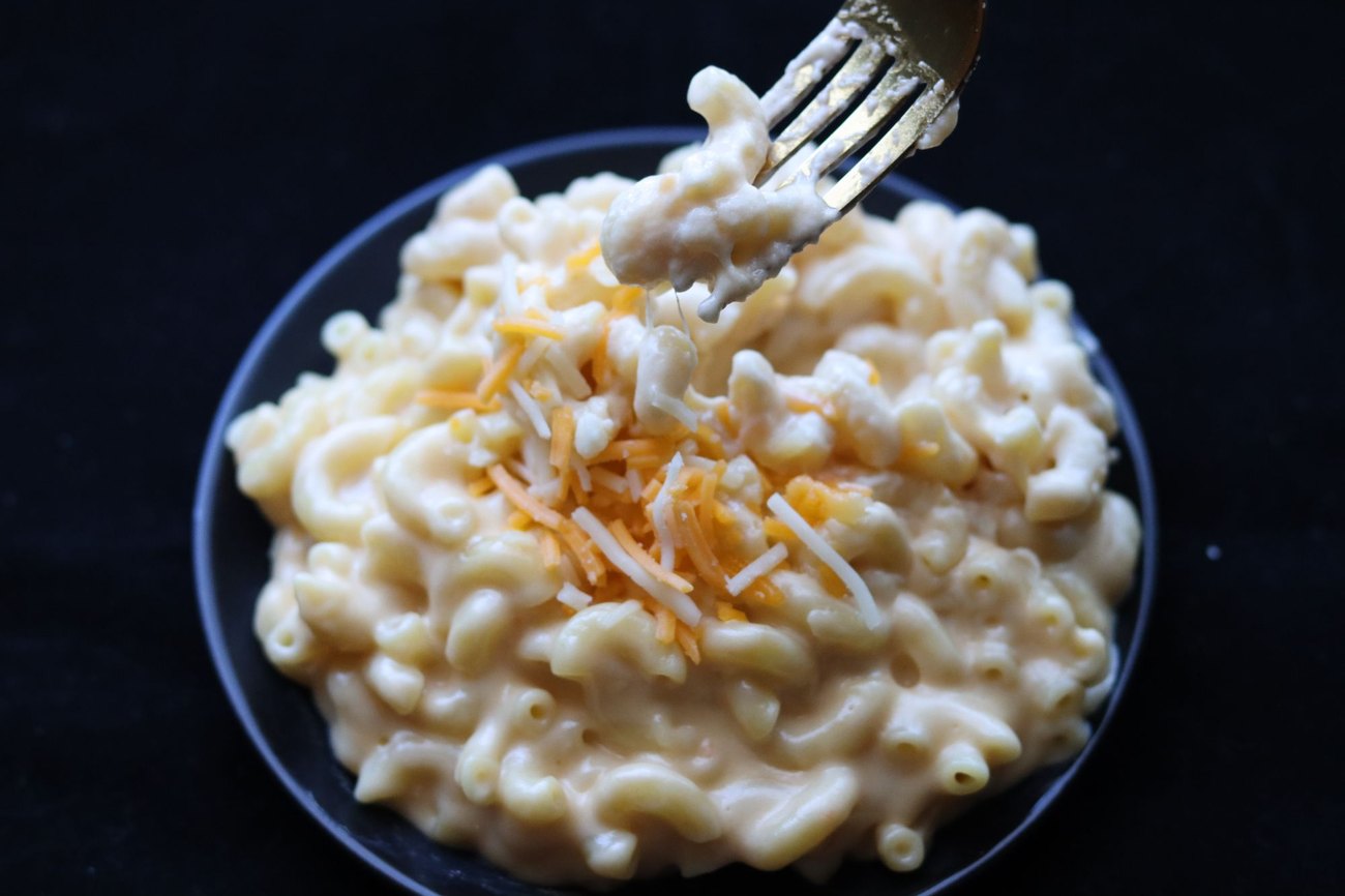 Licensed stock photograph: creamy elbow macaroni and cheese in a dark bowl, shredded cheese over the top.